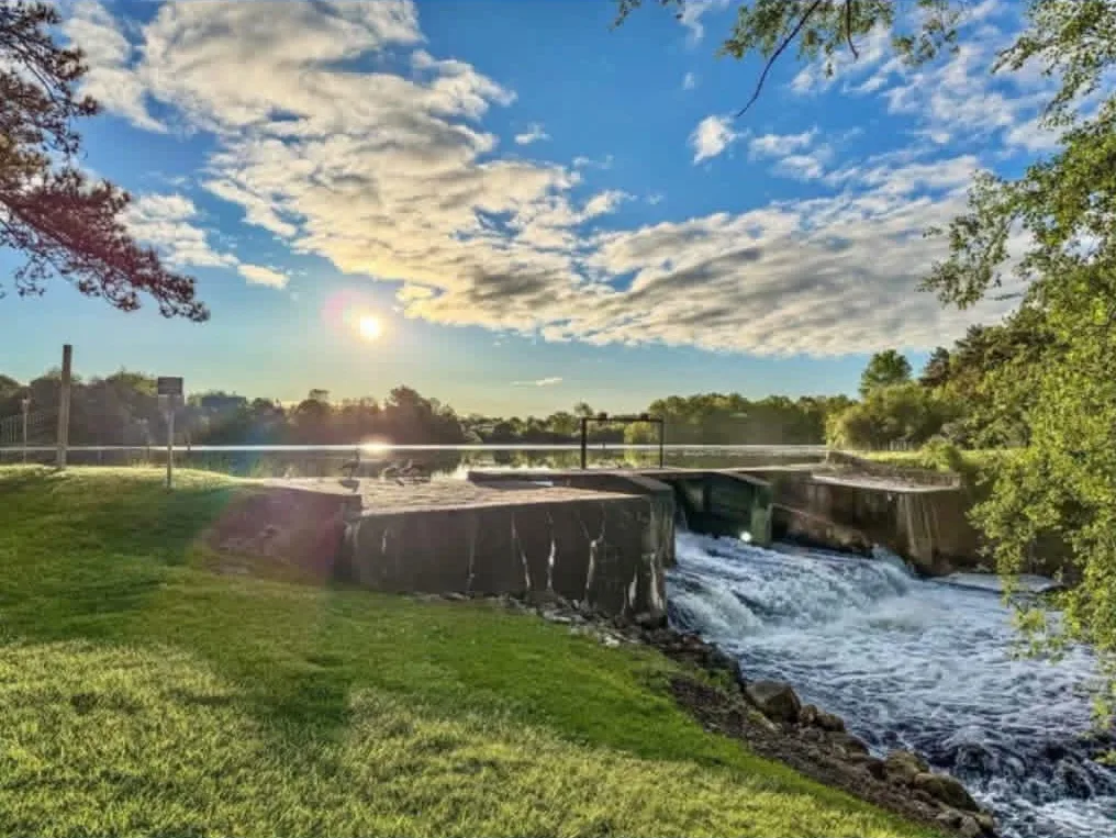 Water rushing over the Stiff’s Mill Pond dam spillway at sunset, with green lawn in the foreground